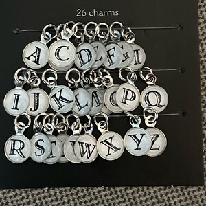 May include: A set of 26 silver charms with white enamel and black letter designs. Each charm features a different letter of the alphabet.