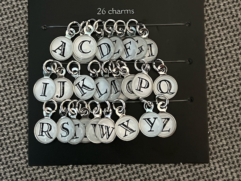 May include: A set of 26 silver charms with white enamel and black letter designs. Each charm features a different letter of the alphabet.