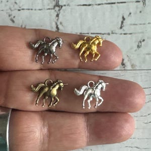 May include: Four small unicorn charms in silver, gold, and bronze tones. The charms are detailed with manes, tails, and horns, and have a loop at the top for attaching to jewelry or other crafts.