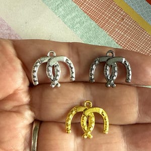 May include: Three silver and gold horseshoe charms. The charms are double-looped and have a textured surface.