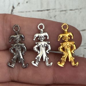 K&ouml;nnte beinhalten: Drei silberne und goldene Narren-Anh&auml;nger mit einem verspielten Design. Die Anh&auml;nger sind in Form eines Narren mit einer spitzen M&uuml;tze, Glocken und einem verspielten Ausdruck.