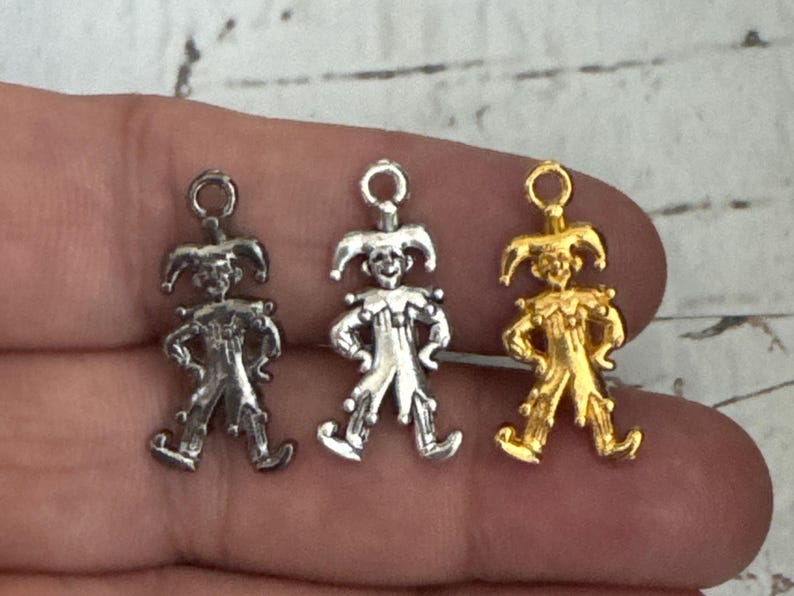 K&ouml;nnte beinhalten: Drei silberne und goldene Narren-Anh&auml;nger mit einem verspielten Design. Die Anh&auml;nger sind in Form eines Narren mit einer spitzen M&uuml;tze, Glocken und einem verspielten Ausdruck.