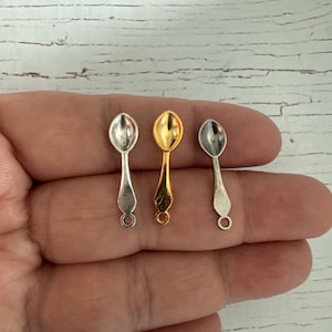 May include: Three miniature spoons in silver, gold, and antique silver finishes. The spoons have a rounded bowl and a simple, elegant handle.
