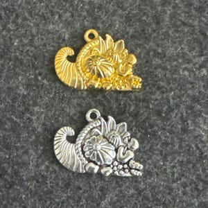 Könnte beinhalten: Zwei Metall-Anhänger in Form eines Füllhorns, einer golden und einer silbern. Beide Anhänger haben ein detailliertes Design mit Blumen und Blättern.