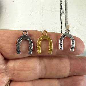 May include: Three silver horseshoe charms with the words "Good Luck" inscribed on them. The charms are in different finishes: silver, gold, and antique silver.