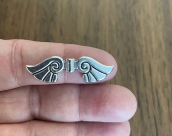 May include: Silver charm with a detailed design of two wings with a decorative swirl pattern.
