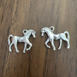 May include: Two silver horse charms, each with a detailed design and a loop for attaching to a necklace or bracelet.