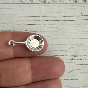 May include: A silver charm in the shape of a small frying pan with a handle.