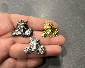 Puede incluir: Tres abalorios de lobo de metal en acabados plateado, dorado y plateado antiguo. Cada abalorio presenta un diseño de lobo detallado con la cola enroscada y una expresión dormida.
