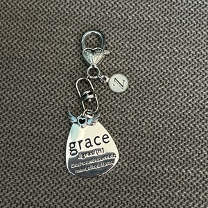 May include: Silver keychain with a teardrop-shaped charm that says "grace /grās/ (n) God's undeserved, unmerited favor". The charm has a small heart and wings on top. The keychain also has a silver letter "Z" charm.