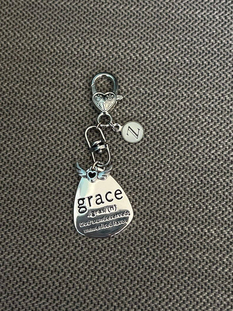 May include: Silver keychain with a teardrop-shaped charm that says "grace /grās/ (n) God's undeserved, unmerited favor". The charm has a small heart and wings on top. The keychain also has a silver letter "Z" charm.
