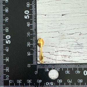 May include: A gold-colored metal spoon charm with a loop at the top for attaching to jewelry or other crafts.