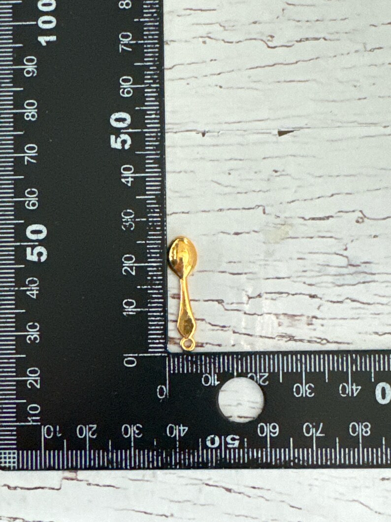 May include: A gold-colored metal spoon charm with a loop at the top for attaching to jewelry or other crafts.