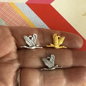 Könnte beinhalten: Drei Vogel-Anhänger aus Silber und Gold, jeder mit einem detaillierten Design eines Vogels im Flug. Die Anhänger sind perfekt, um Schmuck oder Bastelarbeiten mit einem Hauch von Natur zu versehen.