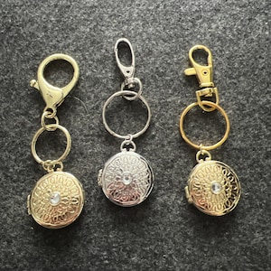 May include: Three gold and silver keychains with round, ornate medallions featuring a clear rhinestone in the center. Each keychain has a different style of clasp.