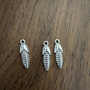 May include: Three silver charm pendants shaped like ears of corn. The charms are detailed with a textured surface to resemble corn kernels.