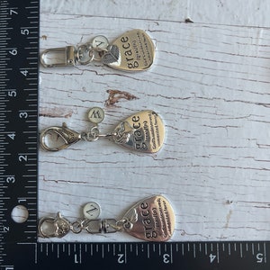 May include: Three silver keychains with a guitar pick charm. Each charm has the word "grace" and a definition of the word. The charms are attached to silver key rings.