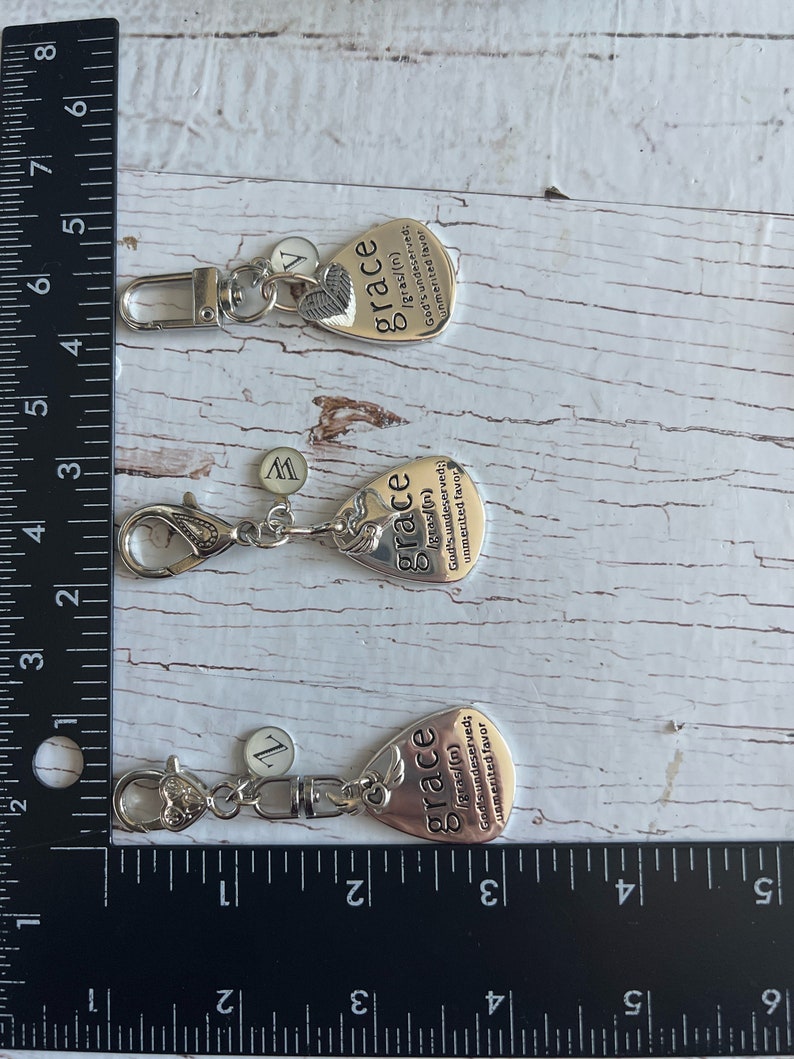 May include: Three silver keychains with a guitar pick charm. Each charm has the word "grace" and a definition of the word. The charms are attached to silver key rings.