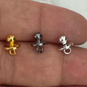 Peut inclure: Trois breloques de sucette en métal doré, argenté et noir.