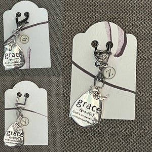 May include: Silver charm with a teardrop-shaped pendant that reads "grace /gras/(n) God's undeserved unmerited favor". The charm is attached to a silver key ring with a small silver heart and a letter "Z" charm.