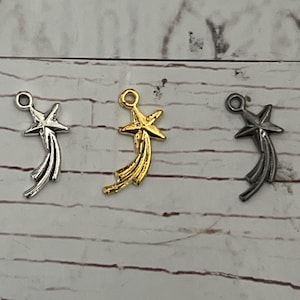 May include: Three shooting star charms in silver, gold, and black metal. Each charm features a five-pointed star at the top of a curved tail.