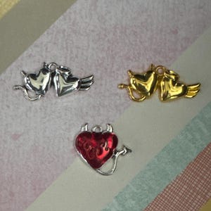 May include: Three silver heart charms with wings and a red heart charm with horns and the word "evil" on it.