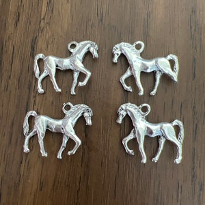 May include: Four silver horse charms, each with a detailed design, perfect for adding a touch of equestrian elegance to jewelry or crafts.