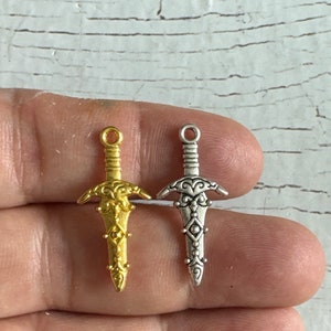 May include: Two ornate sword charms, one gold and one silver, with intricate details and a pointed tip.