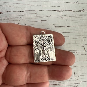 May include: Silver charm pendant featuring a detailed tree of life design. The charm is rectangular in shape and has a textured surface.