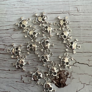 K&ouml;nnte beinhalten: Eine Sammlung silberner Totenkopf-Anh&auml;nger mit Kreuzknochen. Die Anh&auml;nger sind detailliert und perfekt, um Schmuck oder Bastelarbeiten einen Hauch von Gothic-Stil zu verleihen.