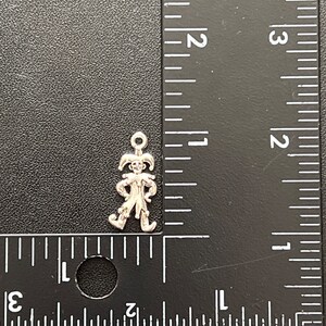 K&ouml;nnte beinhalten: Silberner Anh&auml;nger eines Narren mit spitzen Hut und Gl&ouml;ckchen. Der Anh&auml;nger ist etwa 2,5 cm hoch und wird neben einem Lineal gezeigt.