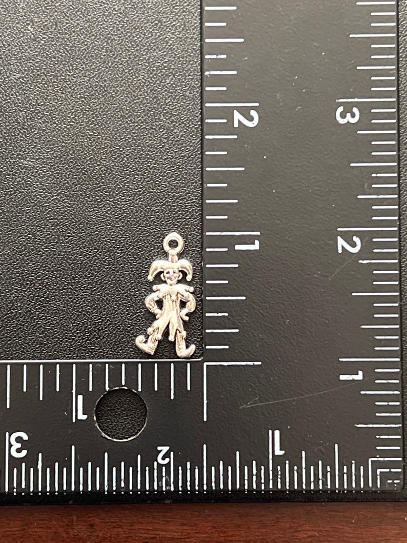 K&ouml;nnte beinhalten: Silberner Anh&auml;nger eines Narren mit spitzen Hut und Gl&ouml;ckchen. Der Anh&auml;nger ist etwa 2,5 cm hoch und wird neben einem Lineal gezeigt.