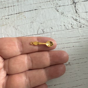 May include: A small gold spoon charm with a loop for attaching to a necklace or bracelet.