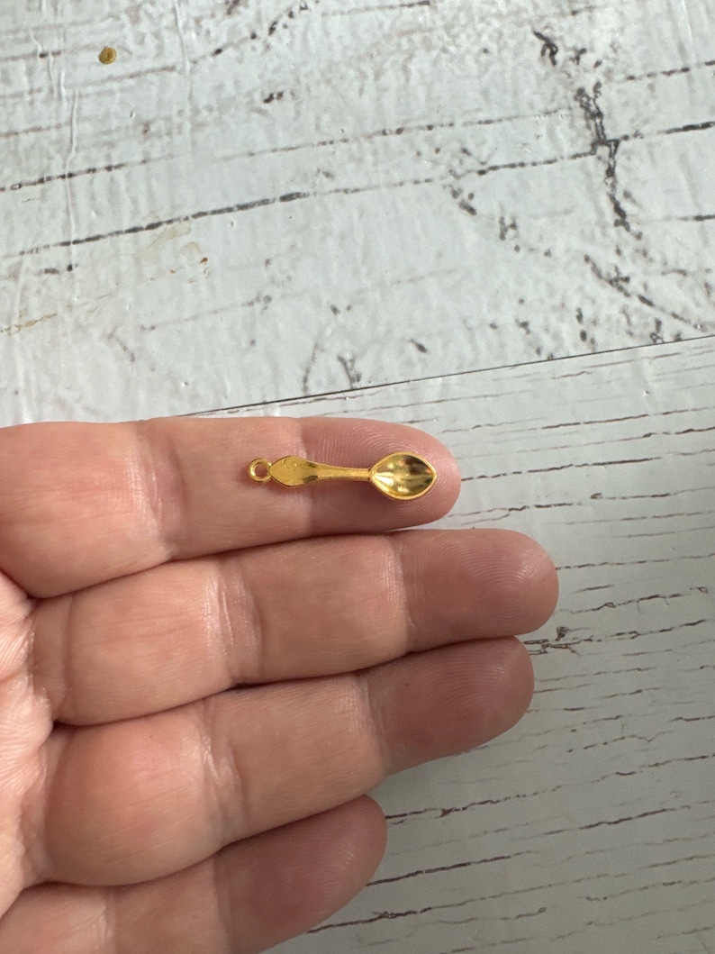 May include: A small gold spoon charm with a loop for attaching to a necklace or bracelet.