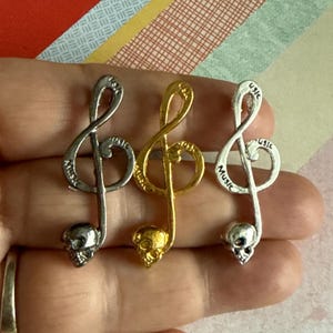May include: Three silver and gold music note charms with a skull at the bottom. The charms are engraved with the word "Music".