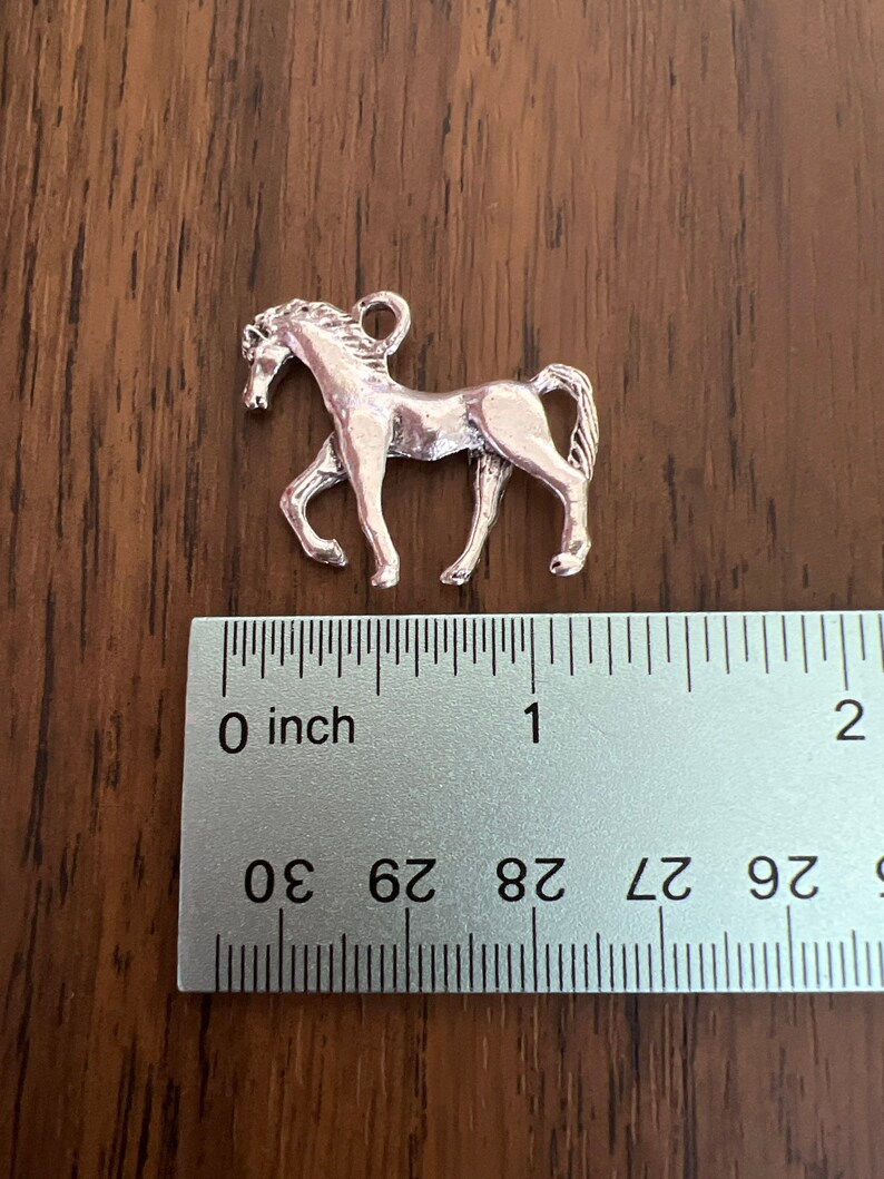 May include: Silver horse charm, approximately 1 inch in length. The charm is detailed with a horse's head, mane, and tail.