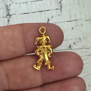K&ouml;nnte beinhalten: Goldfarbener Metall-Anh&auml;nger mit einer Jester-Figur mit spitzen Hut, Gl&ouml;ckchen und einem skurrilen Ausdruck.