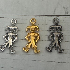 K&ouml;nnte beinhalten: Drei Jester-Anh&auml;nger, einer silber, einer gold und einer schwarz. Jeder Anh&auml;nger ist eine kleine, detaillierte Figur eines Jesters mit Hut und Gl&ouml;ckchen.