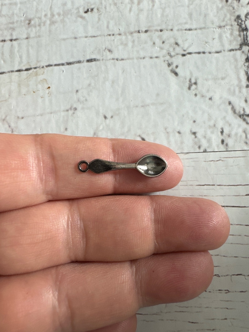 May include: A silver spoon charm with a loop for attaching to a necklace or bracelet.