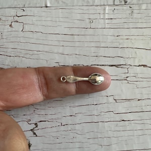 May include: A small silver spoon charm with a loop at the top for attaching to a necklace or bracelet.