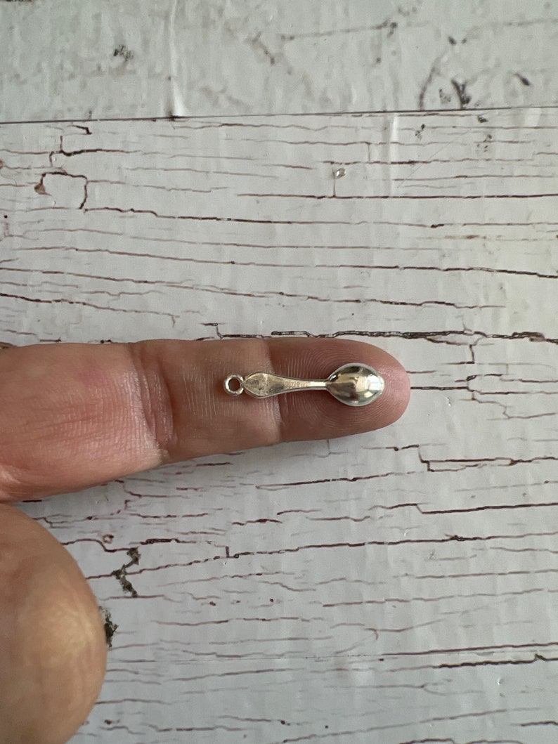 May include: A small silver spoon charm with a loop at the top for attaching to a necklace or bracelet.