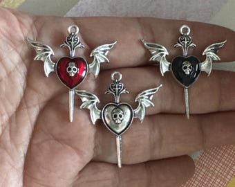 Op de afbeelding: Drie gotische hangers met hartvormige centra, schedeldetails en vleermuisvleugels. De hangers hebben een zilveren afwerking, met een rood, een zwart en een zilver hart. Elke hanger heeft een decoratieve top en een dolkachtige onderkant.