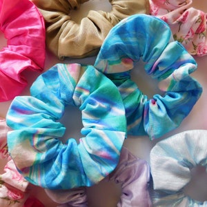 Pode incluir: Uma coleção de scrunchies para cabelo em vários padrões e cores, incluindo rosa, marrom, azul, roxo e branco.