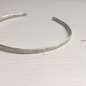May include: A silver hammered bangle bracelet. The bracelet is made from a single piece of metal that has been hammered to create a textured surface.