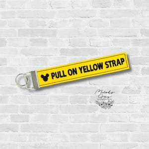 May include: Yellow strap with the text "PULL ON YELLOW STRAP" in black. A black Mickey Mouse head is on the left side of the text. The strap has a silver-colored metal clasp.