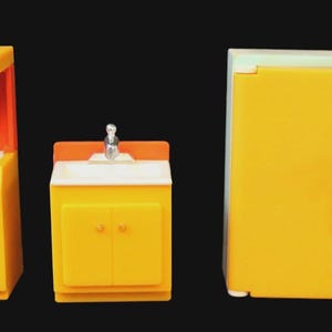 May include: A yellow toy kitchen set with an orange oven, a sink, and a refrigerator. A doll figure with blonde hair, a green apron, and yellow pants stands next to the refrigerator. The set is on a black background.