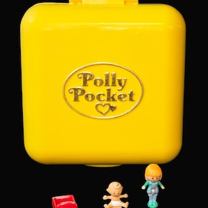 Op de afbeelding: Een felgele Polly Pocket compact met een gouden logo. De compact is gesloten en heeft een rechthoekige vorm met afgeronde hoeken. Drie kleine plastic figuren en een rode auto staan voor de compact.