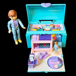 Könnte beinhalten: Ein Vintage-Puppenhaus-Spielset in Blau-, Rosa- und Lilatönen mit einem Miniatur-Schlafzimmer, einem Schreibtisch und einem Schaukelpferd. Eine Puppe in einem blauen Outfit steht daneben. Das Spielset ist etwa 10 cm breit.