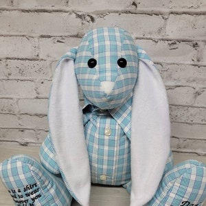 May include: A blue and white plaid bunny rabbit stuffed animal with white felt ears. The bunny is wearing a blue and white plaid shirt with a button closure. The bunny's feet are embroidered with the text "Dad 8/16/59" and "This is a shirt I'd to wear whenever you hold it know that I am there".