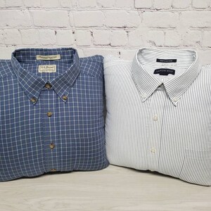 May include: Two button-down shirts, one blue plaid and one white with thin gray stripes. Both shirts are folded and arranged as pillows.